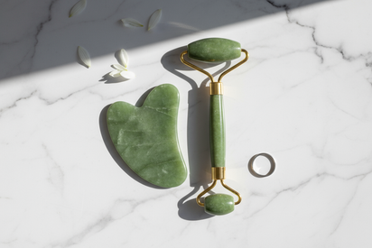 Aesthetic photo showing a green jade gua sha and roller on a marble background