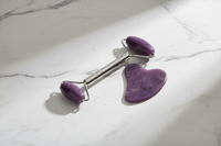 Elegant product photo of a purple facial massage roller and heart-shaped gua sha on a marble table